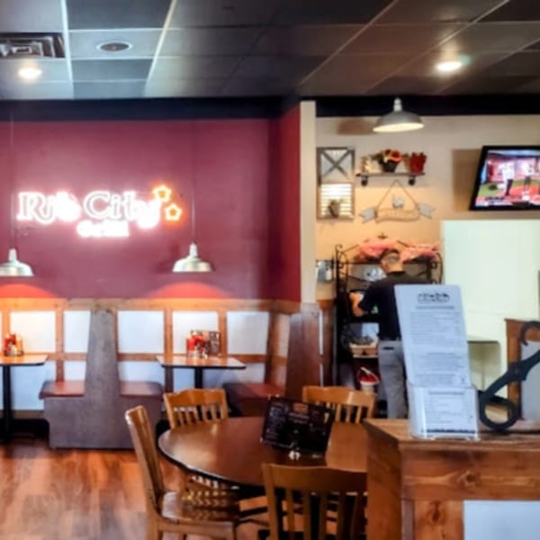 Interior of Rib City restaurant with neon sign, booths, tables, and a person working behind a counter.