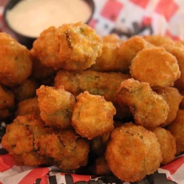 A close-up of golden-brown fried okra with a side of dipping sauce in a black bowl.