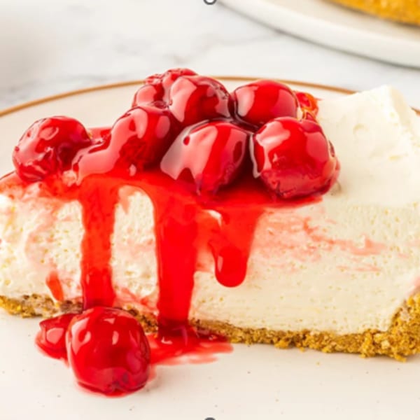 A slice of cheesecake with a graham cracker crust, topped with bright red cherry pie filling.