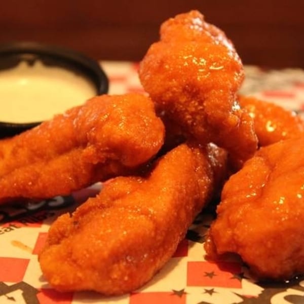 Close-up of several orange-glazed chicken wings with a side of ranch dressing on a checkered paper.