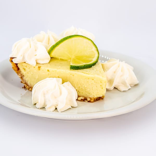 A slice of Key Lime Pie with whipped cream and a lime wedge on a white plate.