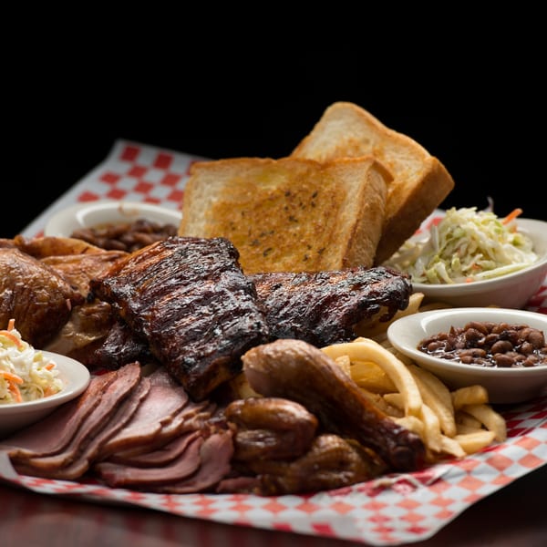 A large platter of Rib City BBQ with ribs, sliced meat, chicken, fries, coleslaw, and baked beans.