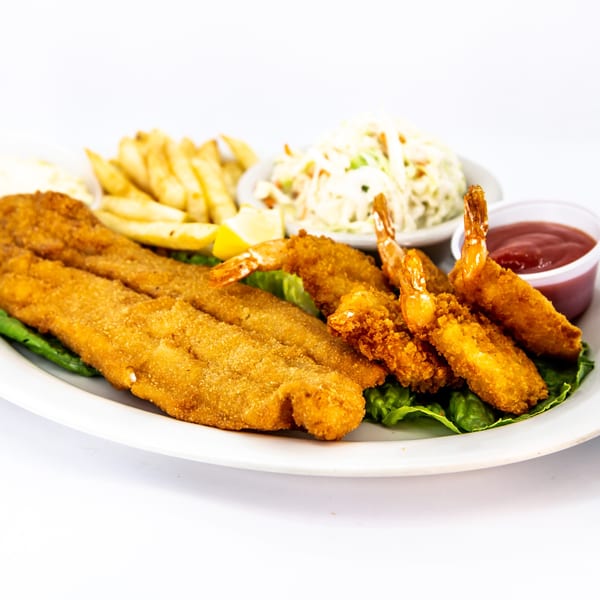 Fried fish and shrimp platter with french fries, coleslaw, lemon, and ketchup on a white plate.