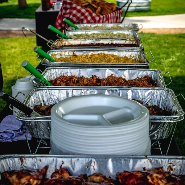 Rib City BBQ buffet with pulled pork, ribs, mac and cheese, and other sides in foil trays.