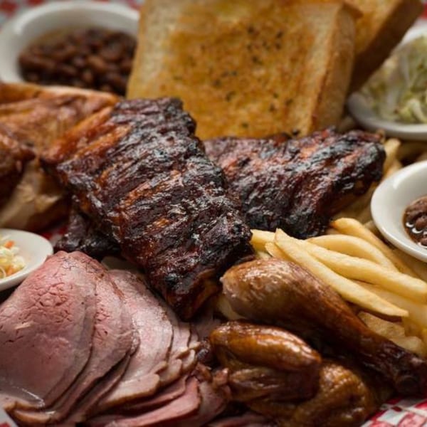A large platter of Rib City BBQ with ribs, sliced beef, chicken, fries, baked beans, and toast.
