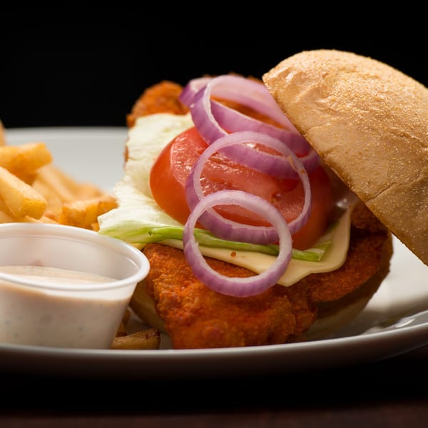 Crispy chicken sandwich with lettuce, tomato, onion, cheese, fries, and dipping sauce.