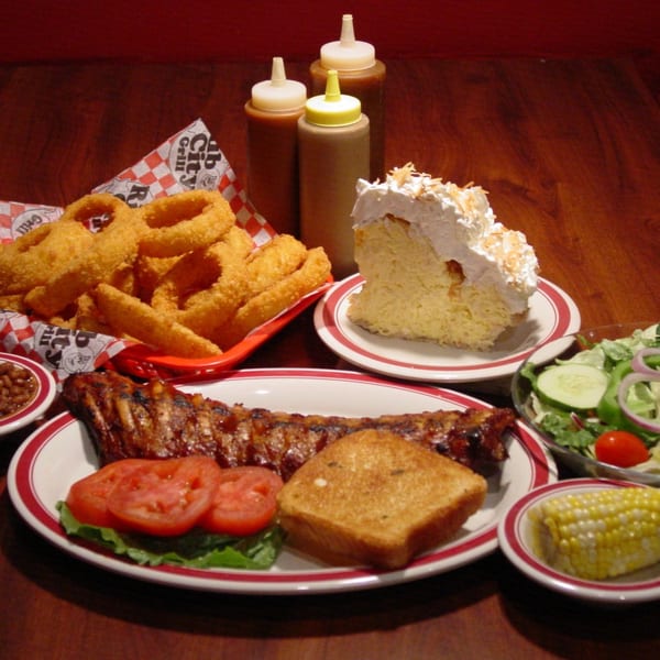 A Rib City BBQ feast with ribs, onion rings, salad, corn, baked beans, toast, and cake.