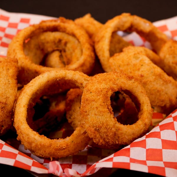 A basket of golden-brown, crispy Rib City onion rings on red and white checkered paper.