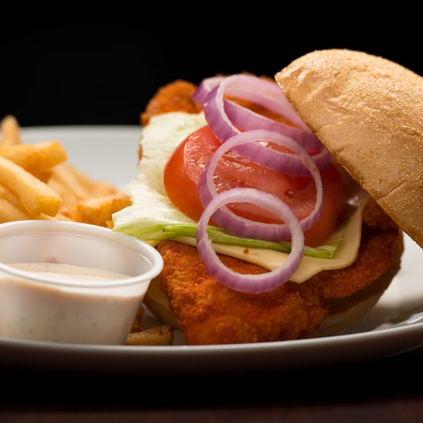 Rib City's crispy chicken sandwich with lettuce, tomato, red onion, cheese, fries, and dipping sauce.